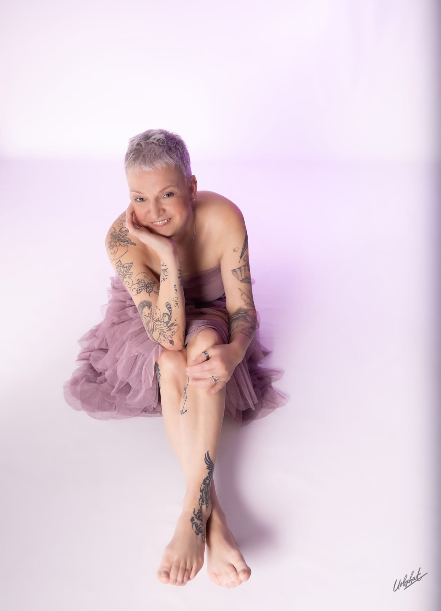 Katlui — Glamour look: lavender tulle dress, seated portrait with hand resting under chin, visible tattoos